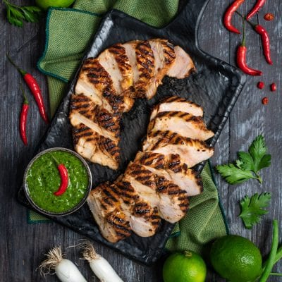 Pollo marinato alla griglia affettato, servito con salsa chimichurri verde e peperoncino