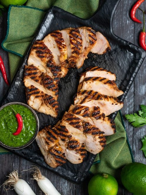Pollo marinato alla griglia affettato, servito con salsa chimichurri verde e peperoncino