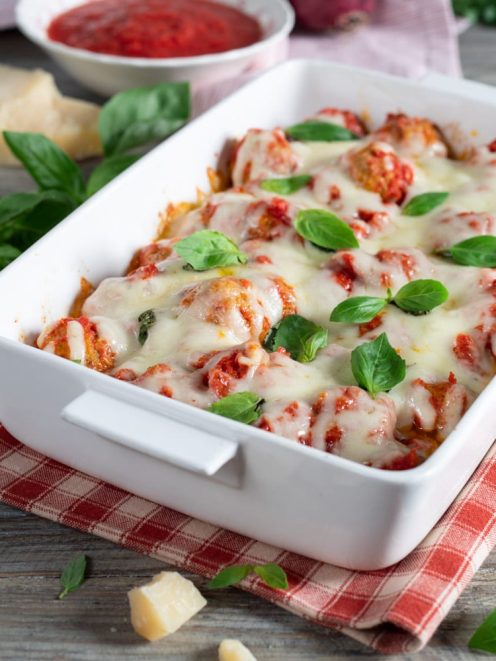 Polpette filanti al sugo coperte di mozzarella fusa e foglie di basilico fresco