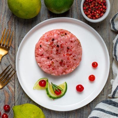 Tartare di vitello modellata a disco, con pepe rosa, lime a spicchi e bacche rosse