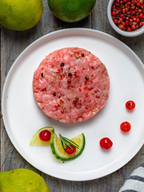 Tartare di vitello modellata a disco, con pepe rosa, lime a spicchi e bacche rosse