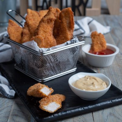 Chicken tender croccanti serviti con salsa alla senape e ketchup, uno spezzato mostra l'interno morbido