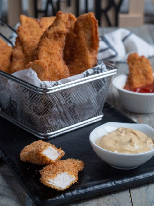 Chicken tender croccanti serviti con salsa alla senape e ketchup, uno spezzato mostra l'interno morbido