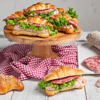 Cornetti salati soffici farciti con salame, lattuga e crema di carne, cosparsi di semi di sesamo