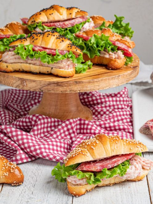 Cornetti salati soffici farciti con salame, lattuga e crema di carne, cosparsi di semi di sesamo