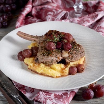 Costolette di vitello con uva su letto di polenta cremosa, guarnite con timo fresco e fondo di cottura