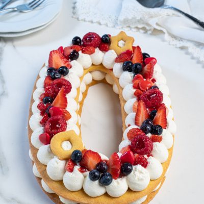 Number cake a forma di zero con ciuffi di panna, fragole, lamponi e mirtilli freschi