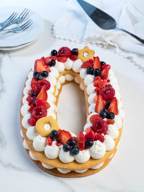 Number cake a forma di zero con ciuffi di panna, fragole, lamponi e mirtilli freschi