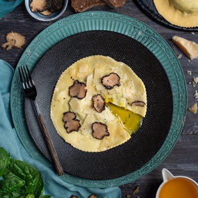 Raviolone con tuorlo fondente aperto, lamelle di tartufo nero e scaglie di parmigiano