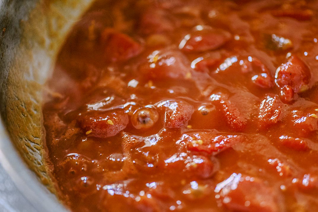 Pomodori a pezzi che sobbollono in padella formando un sugo denso e lucido