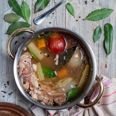 Brodo di carne in cottura con sedano, carota, pomodoro, alloro e grani di pepe