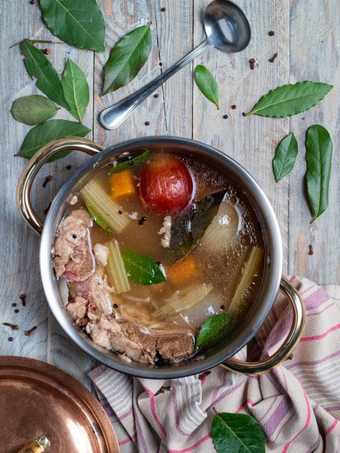 Brodo di carne in cottura con sedano, carota, pomodoro, alloro e grani di pepe