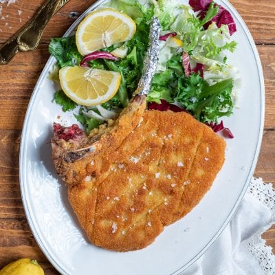 Costoletta alla milanese con osso, panatura dorata e sale in scaglie, servita con insalata mista e fette di limone