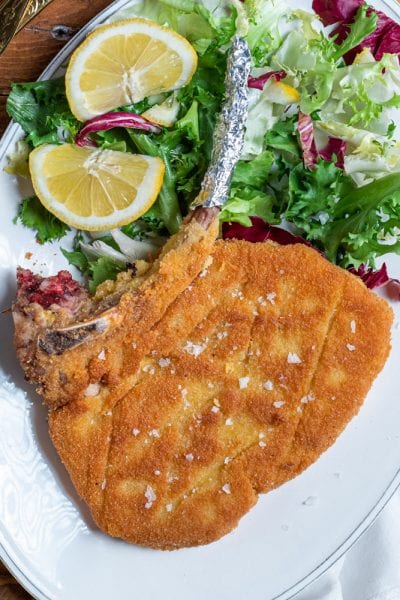 Costoletta alla milanese con osso, panatura dorata e sale in scaglie, servita con insalata mista e fette di limone