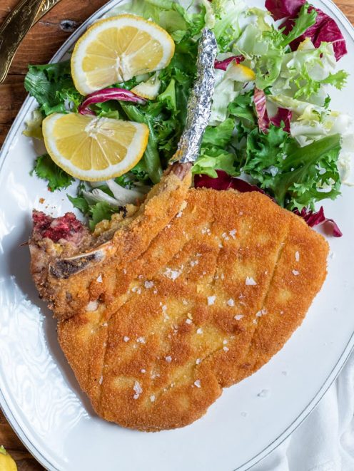 Costoletta alla milanese con osso, panatura dorata e sale in scaglie, servita con insalata mista e fette di limone