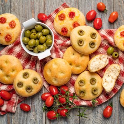 Focaccine morbide con olive verdi e pomodorini, alcune spezzate a metà per mostrare la mollica soffice