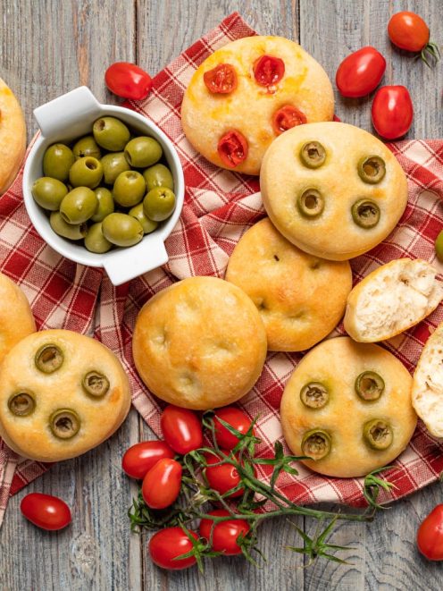 Focaccine morbide con olive verdi e pomodorini, alcune spezzate a metà per mostrare la mollica soffice