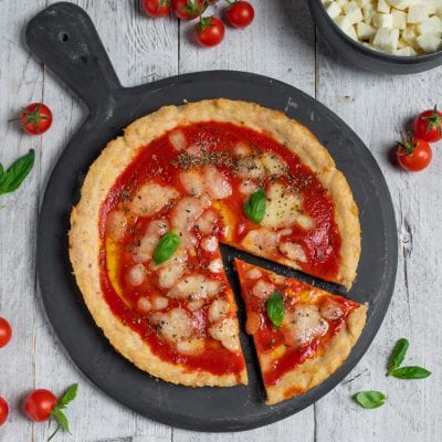 Pizza di tacchino con salsa di pomodoro, mozzarella sciolta e foglie di basilico fresco, una fetta già tagliata
