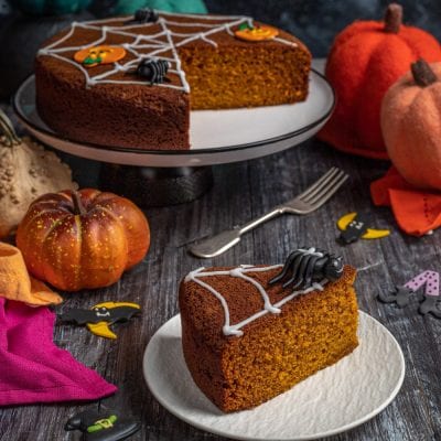 Torta di zucca speziata decorata con ragnatela di glassa bianca e ragno di zucchero, una fetta in primo piano