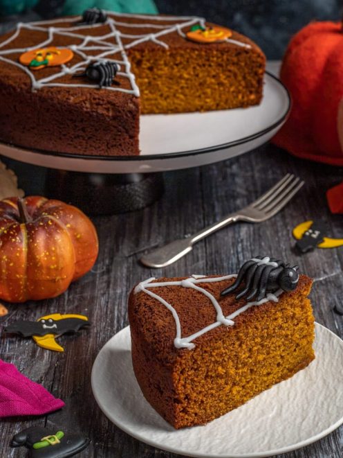 Torta di zucca speziata decorata con ragnatela di glassa bianca e ragno di zucchero, una fetta in primo piano