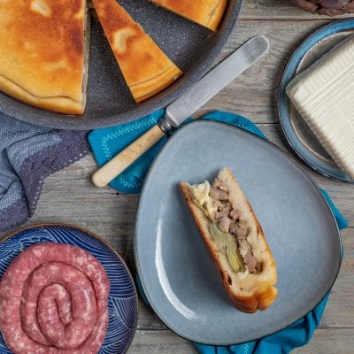 Focaccia in padella ripiena tagliata a metà con salsiccia, carciofi e formaggio fuso