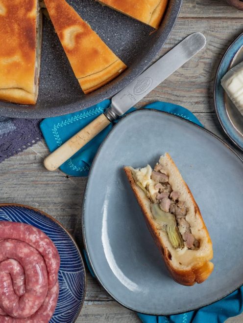 Focaccia in padella ripiena tagliata a metà con salsiccia, carciofi e formaggio fuso