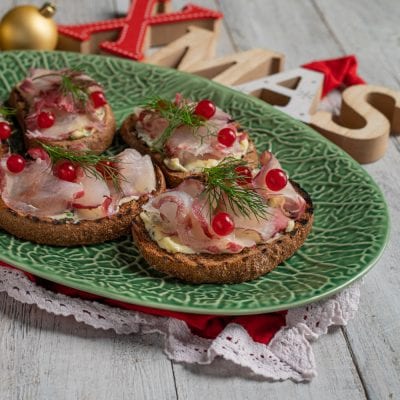 Gravlax di branzino su crostini di pane nero con burro, ribes rosso e ciuffi di aneto