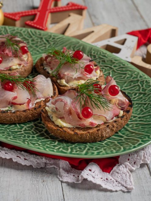 Gravlax di branzino su crostini di pane nero con burro, ribes rosso e ciuffi di aneto