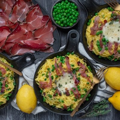 Nidi di tagliolini con speck croccante, piselli e fonduta al centro serviti in padelline