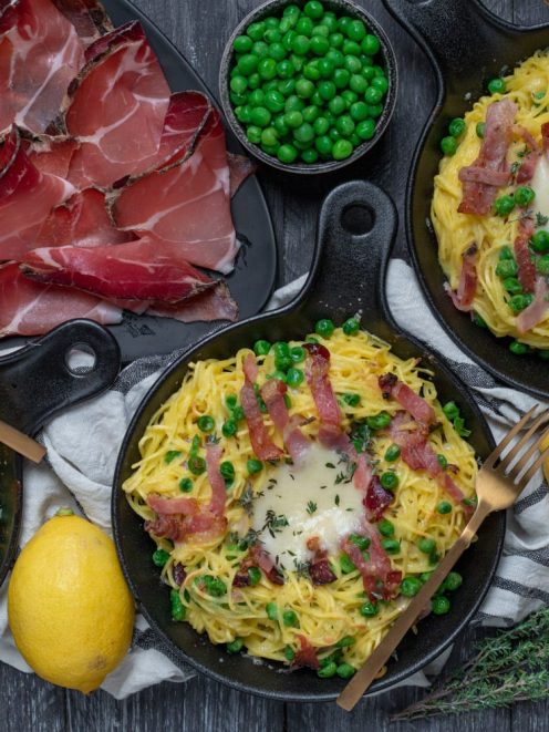 Nidi di tagliolini con speck croccante, piselli e fonduta al centro serviti in padelline