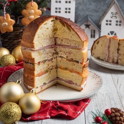 Panettone gastronomico farcito a strati con salumi, formaggi cremosi e verdure grigliate, tagliato a meta