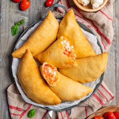 Panzerotti pugliesi fritti con ripieno di pomodoro e mozzarella, uno aperto in primo piano