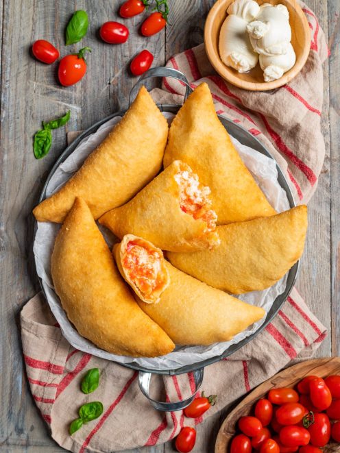 Panzerotti pugliesi fritti con ripieno di pomodoro e mozzarella, uno aperto in primo piano