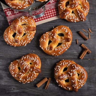Bretzel dolci glassati e ricoperti di granella di zucchero disposti su tavola di legno con cannella