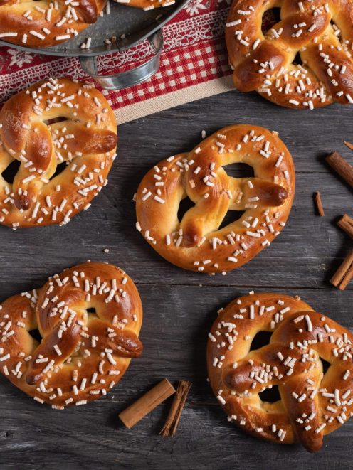Bretzel dolci glassati e ricoperti di granella di zucchero disposti su tavola di legno con cannella