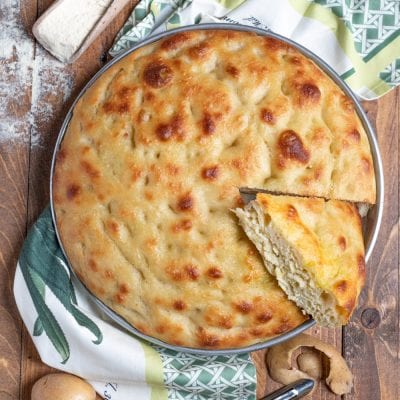 Focaccia di patate dorata e soffice con una fetta sollevata che mostra la mollica
