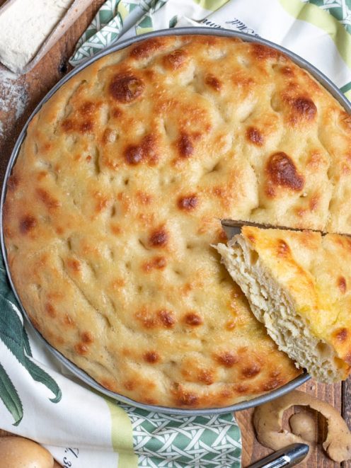 Focaccia di patate dorata e soffice con una fetta sollevata che mostra la mollica