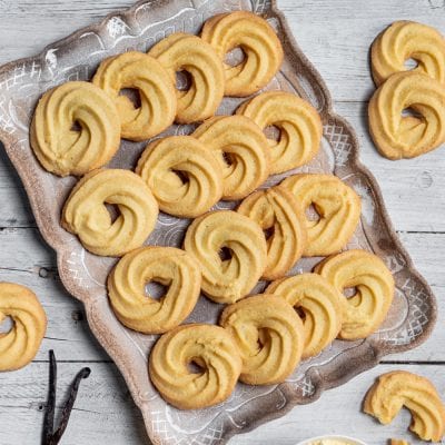 Paste di meliga a forma di ricciolo disposte su un vassoio accanto a bacche di vaniglia
