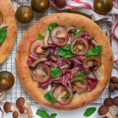 Pizza con carne salada, funghi pioppini, pomodori e basilico fresco appena sfornata