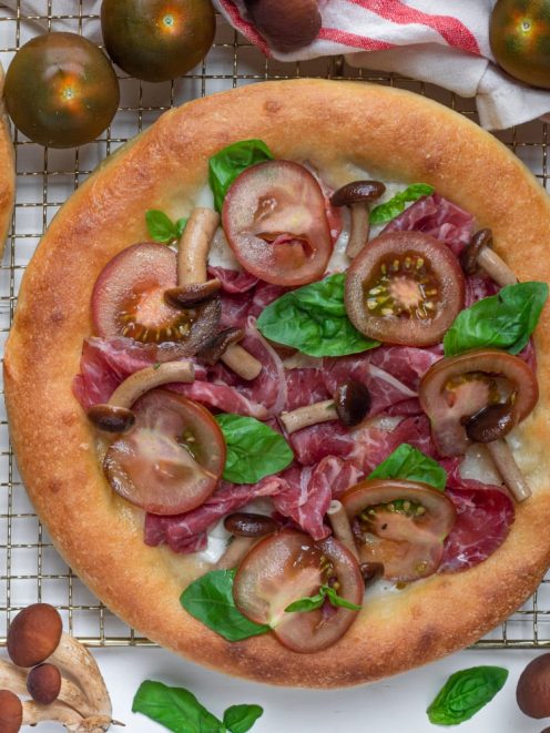Pizza con carne salada, funghi pioppini, pomodori e basilico fresco appena sfornata