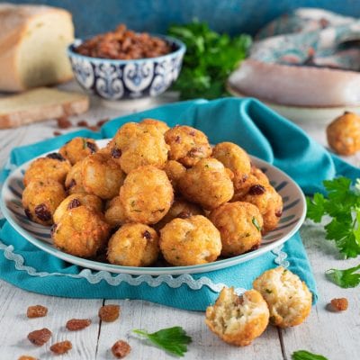 Polpettine di baccalà fritte dorate, con uvetta e prezzemolo, una spezzata rivela l'interno morbido