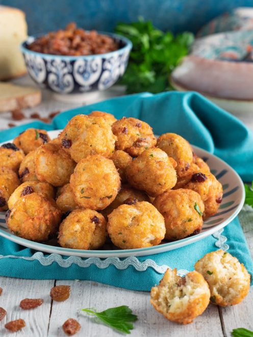 Polpettine di baccalà fritte dorate, con uvetta e prezzemolo, una spezzata rivela l'interno morbido