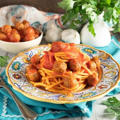 Spaghettoni al sugo con polpettine di alici disposti su piatto decorato accanto a una ciotola di polpettine