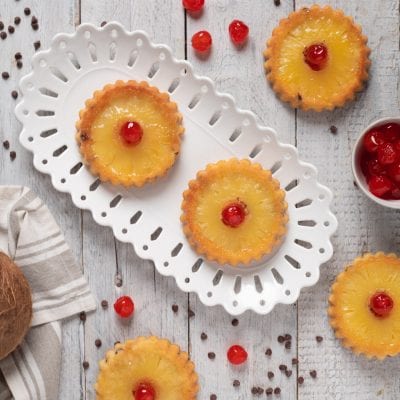 Tortine cocco ananas e gocce cioccolato guarnite con ciliegie candite su fette di ananas caramellate