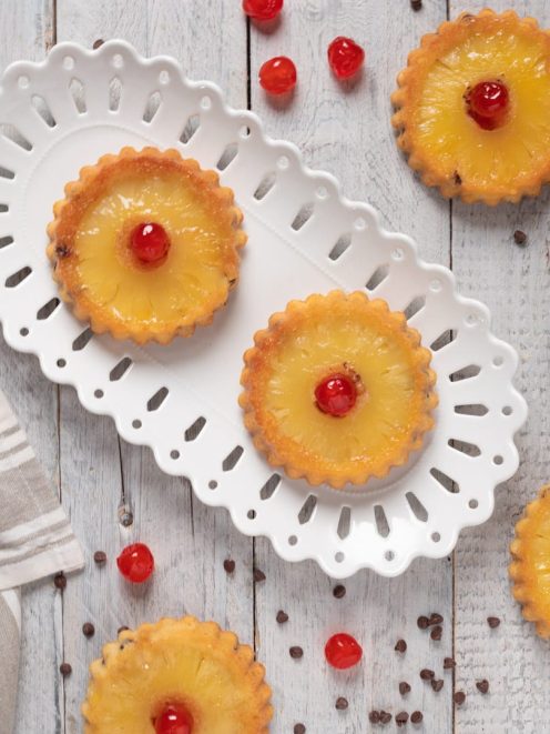 Tortine cocco ananas e gocce cioccolato guarnite con ciliegie candite su fette di ananas caramellate