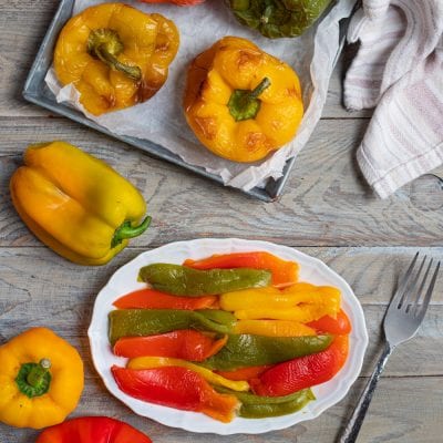 Peperoni arrostiti su teglia e peperoni a filetti, rossi, gialli e verdi su piatto di portata.