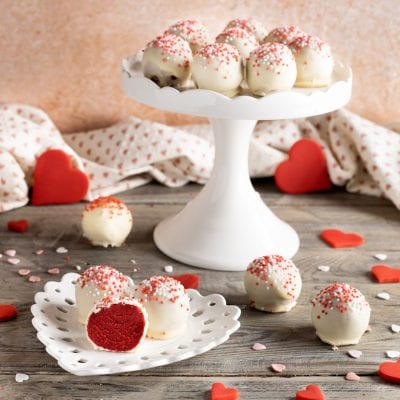 Red velvet bites ricoperti di cioccolato bianco e codette colorate, uno tagliato a meta con cuore rosso in vista