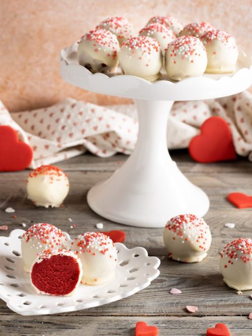 Red velvet bites ricoperti di cioccolato bianco e codette colorate, uno tagliato a meta con cuore rosso in vista