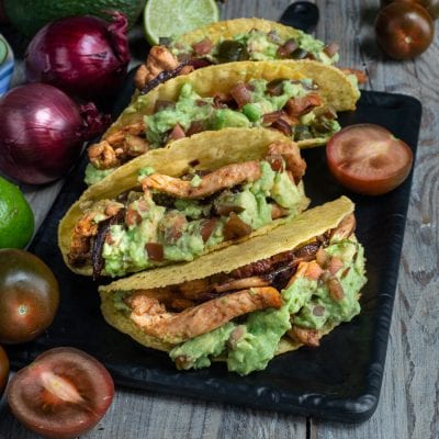 Tacos con pollo e guacamole in guscio di mais farciti con strisce di pollo grigliato e cipolla caramellata
