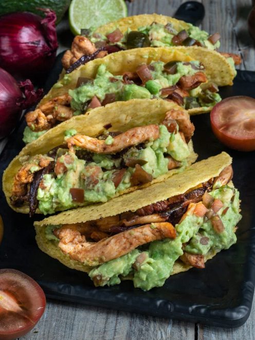Tacos con pollo e guacamole in guscio di mais farciti con strisce di pollo grigliato e cipolla caramellata